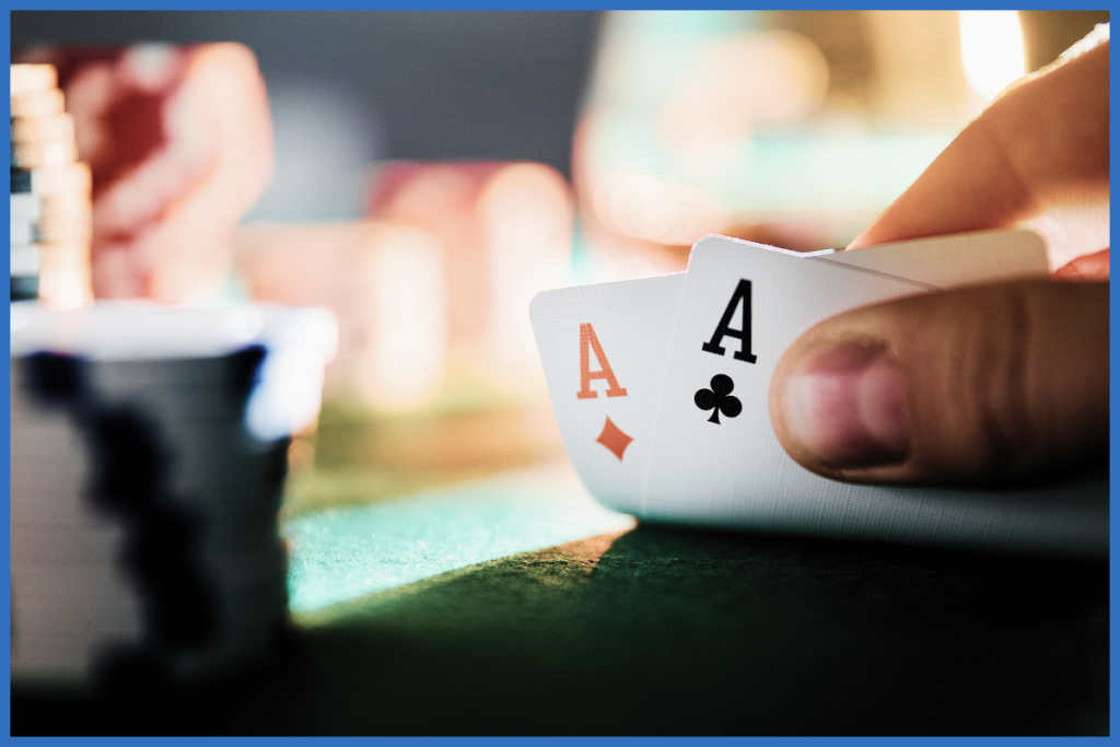 A poker player lifts the corner of their cards to reveal two Aces (a diamond and a club).
